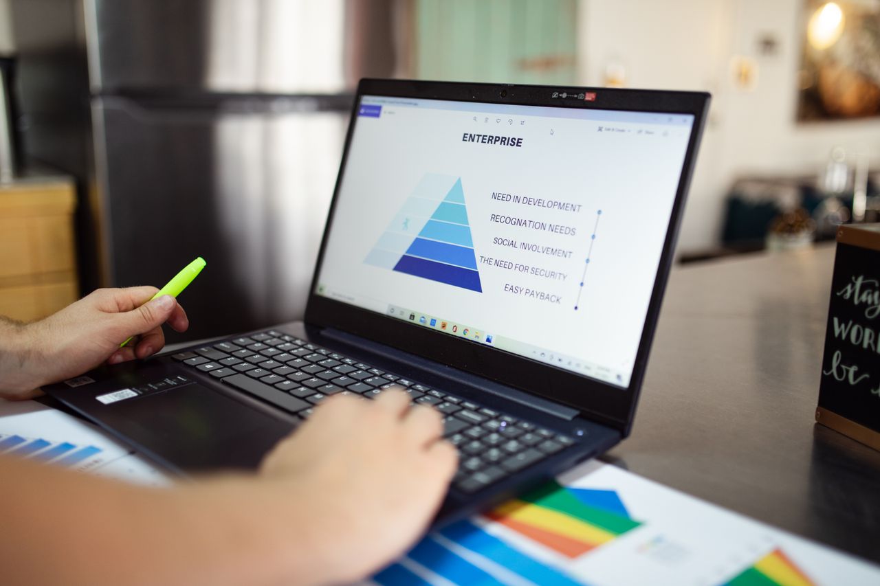 about-img Person analyzes business data on laptop, using pyramid chart and financial reports.